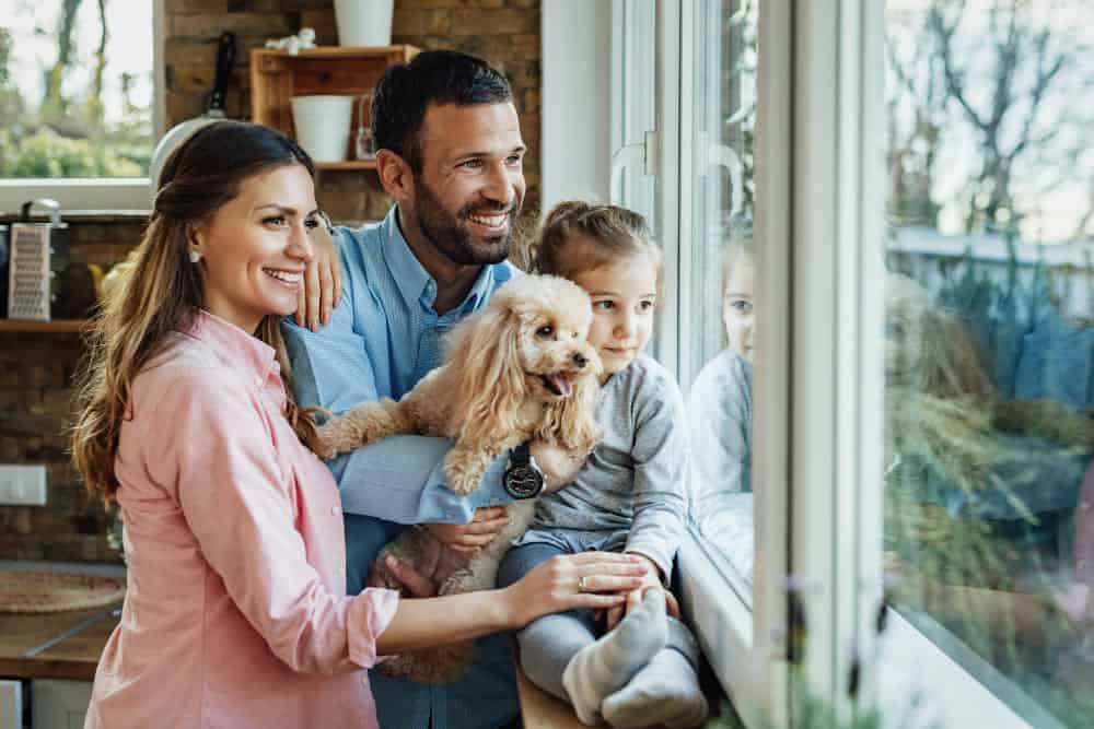 Glückliche Familie mit Hund, die dank eines Immobilienmaklers ihr neues Zuhause genießt.