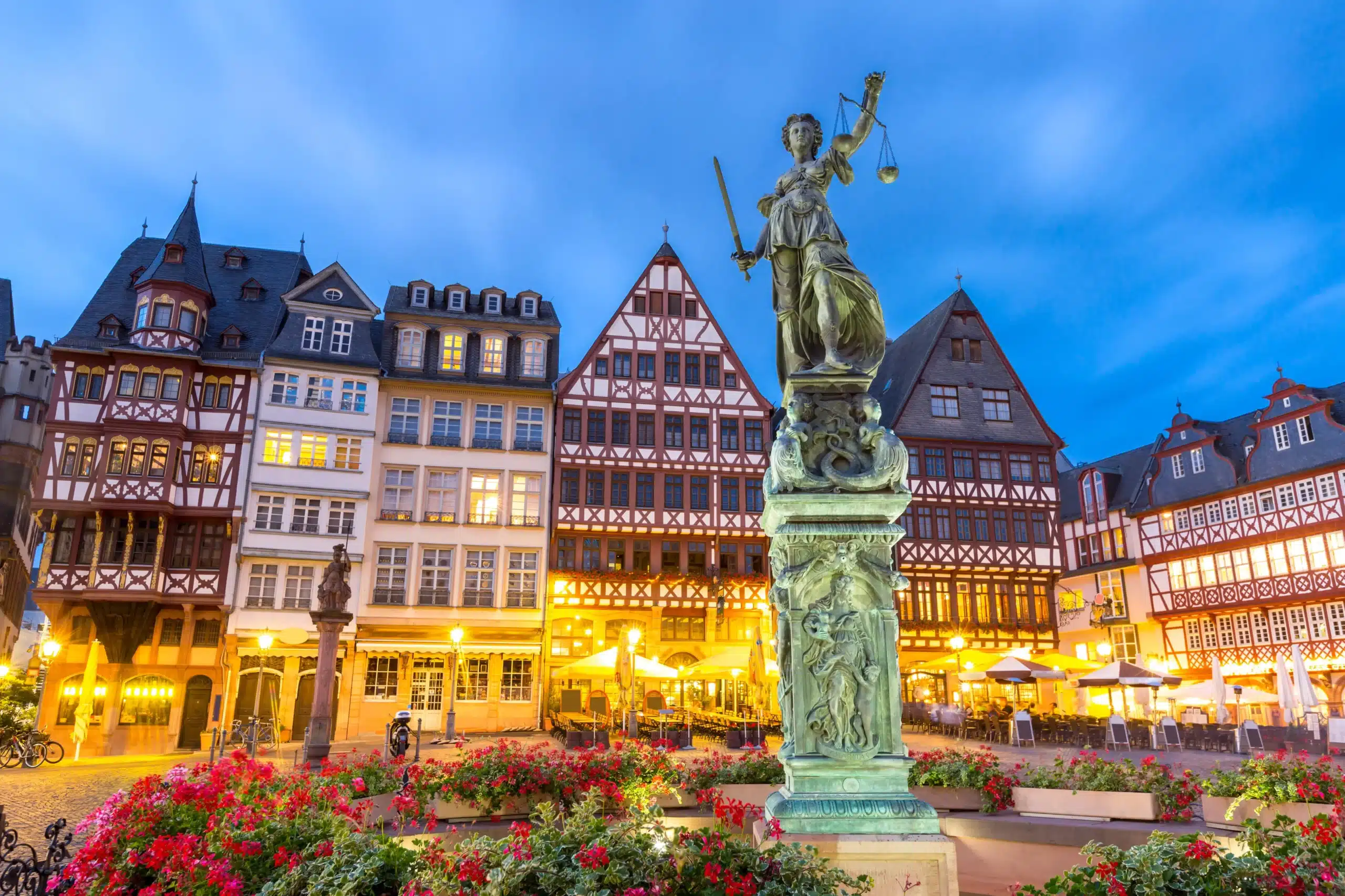 Malerische Fachwerkhäuser und die Justitia-Statue in der beleuchteten Frankfurter Altstadt bei Dämmerung. Perfekt für Immobilienmakler Frankfurt.