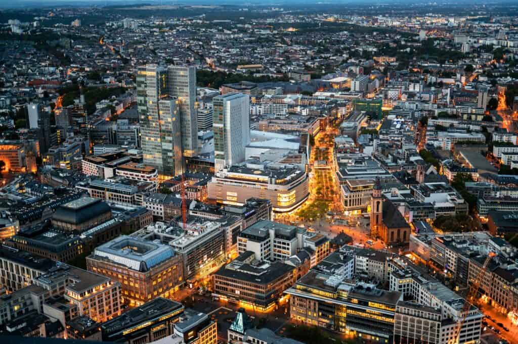 Luftaufnahme der beleuchteten Frankfurter Innenstadt mit ihren modernen Hochhäusern und geschäftigen Straßen bei Sonnenuntergang. Perfekt für Immobilienmakler Frankfurt.