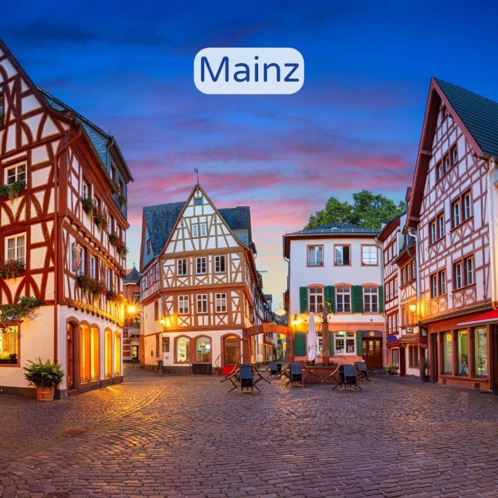 Malerische Gasse in Mainz bei Abenddämmerung mit beleuchteten Geschäften und Kopfsteinpflaster.