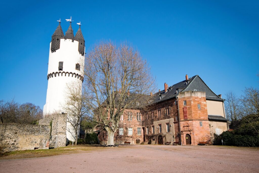 Historische Burg mit einem markanten weißen Turm neben einem alten, sandsteinfarbenen Herrenhaus in Hanau, ideal für Immobilienmakler, die einzigartige Immobilien vermarkten.