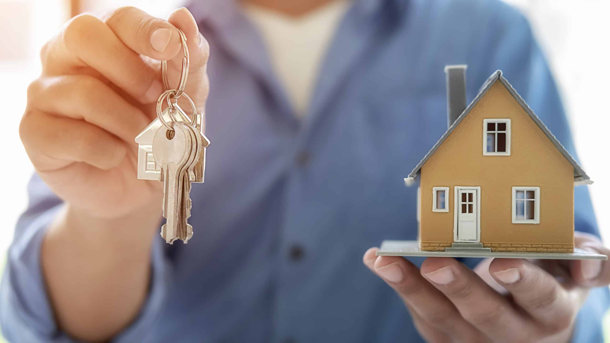 Ein Immobilienmakler übergibt einen Schlüsselbund und hält ein Modellhaus in der Hand, symbolisiert den erfolgreichen Immobilienverkauf und die professionelle Betreuung durch Immobilienmakler in Bad Nauheim.