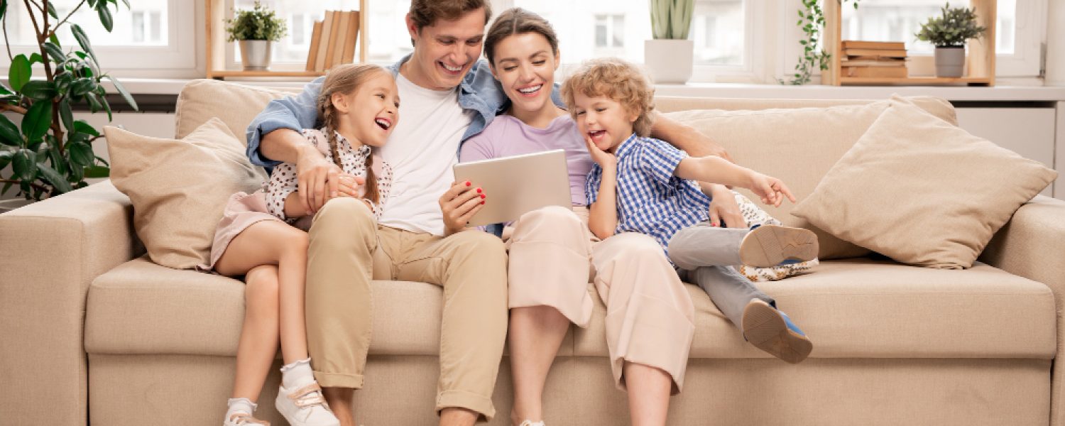 young-joyful-casual-family-two-kids-couple-sitting-sofa-watching-funny-video young-joyful-casual-family-two-kids-couple-sitting-sofa-watching-funny-video